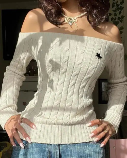 Model wearing white off-shoulder cable-knit sweater with embroidered horse logo, blue jeans and a bow necklace