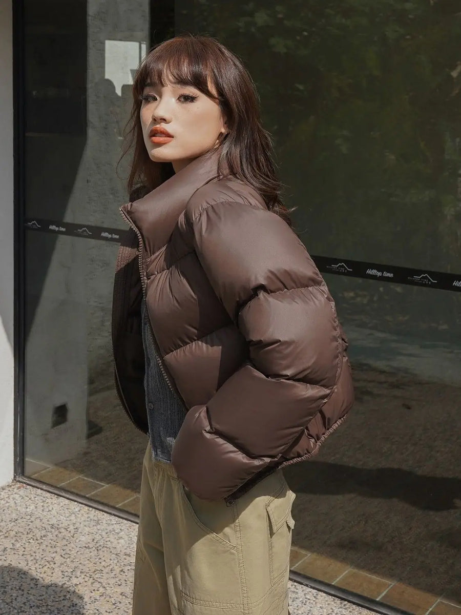 Woman wearing a brown cropped puffer jacket standing outside a building