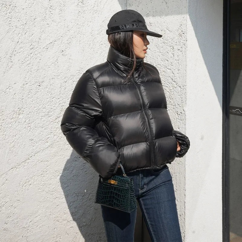 Woman wearing a cropped puffer jacket with black jeans and a cap against a textured wall