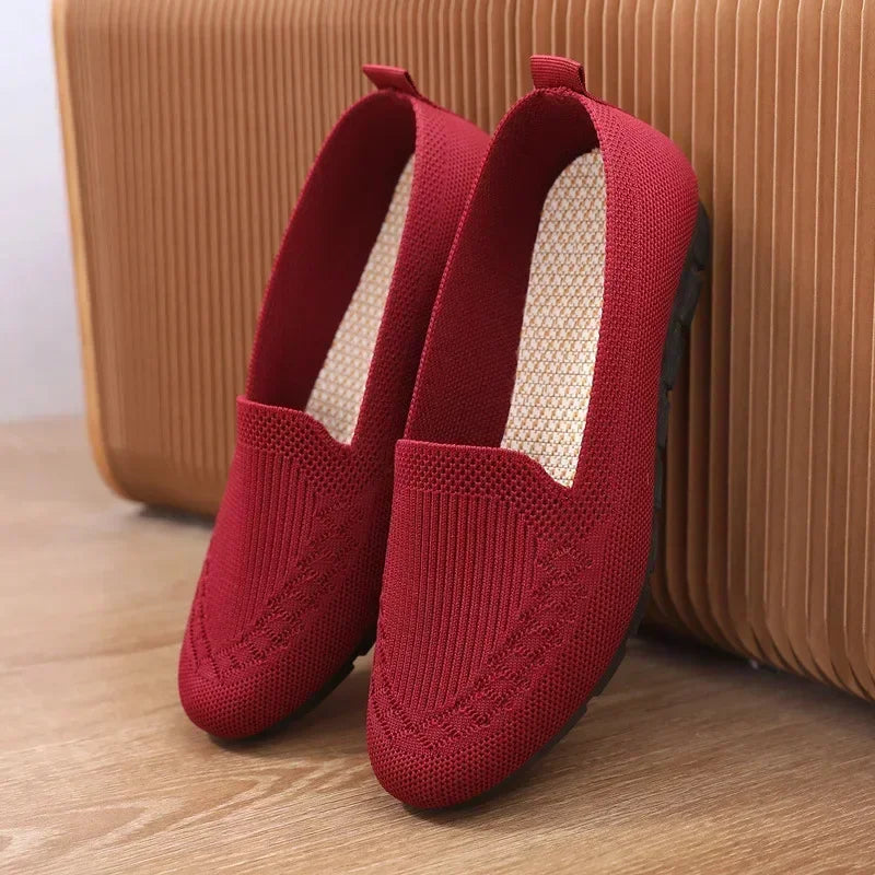 Red loafers on a wooden floor with a brown suitcase in the background