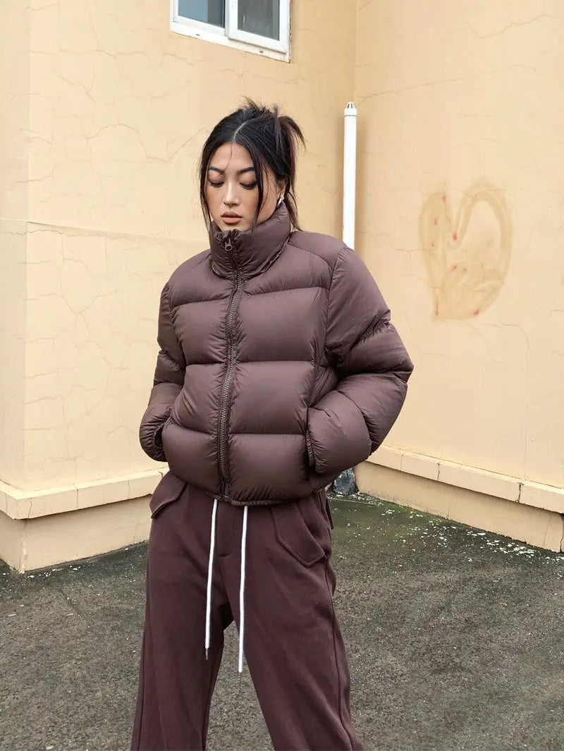 Person wearing a brown cropped puffer jacket and pants standing against a beige wall