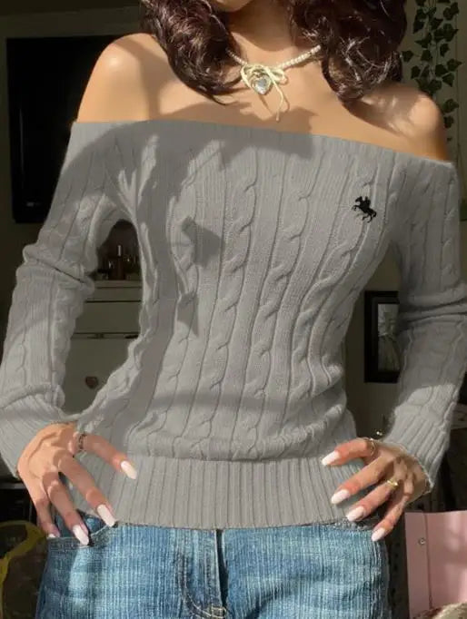 Model wearing light gray off-shoulder cable-knit sweater with embroidered horse logo, blue jeans and a bow necklace