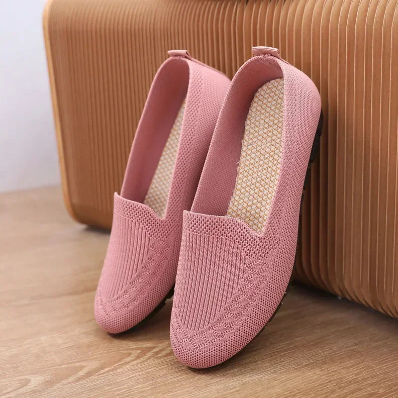 Pink loafers on a wooden floor with a brown suitcase in the background