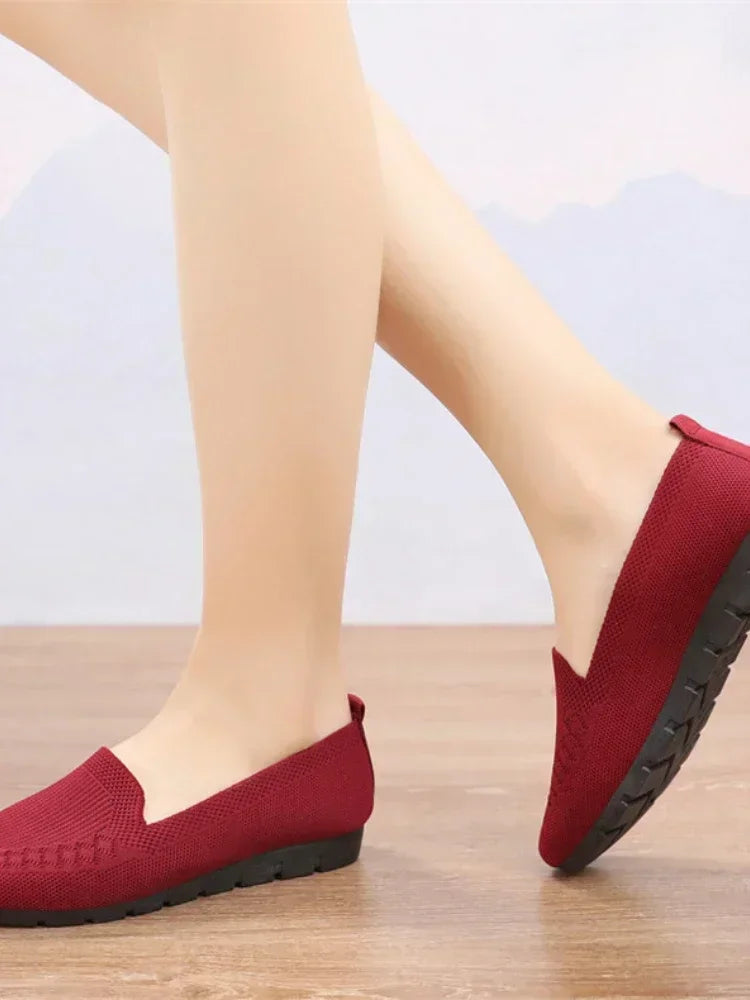 Red loafers worn with light-colored pants on a wooden floor.