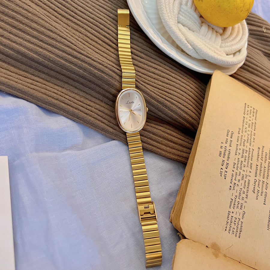 Gold watch on a textured surface with a book and lemon