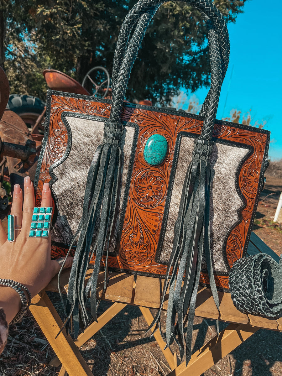 Handcrafted leather bag with braided handles and turquoise stone, outdoors.