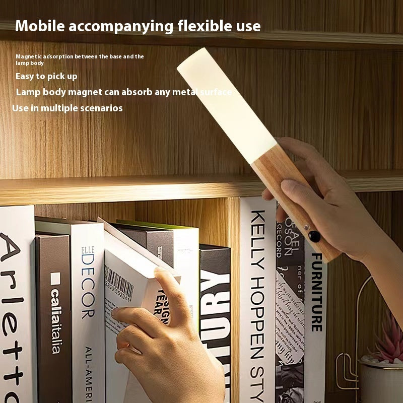 Hand holding the wood grain magnetic motion sensor night light over books on a shelf
