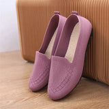 Pair of purple loafers on a wooden floor with a brown suitcase in the background.