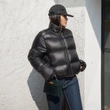 Woman wearing a cropped puffer jacket with black jeans and a cap against a textured wall