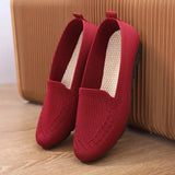 Red loafers on a wooden floor with a brown suitcase in the background