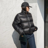 Person wearing a black cropped puffer jacket and cap against a light-colored wall