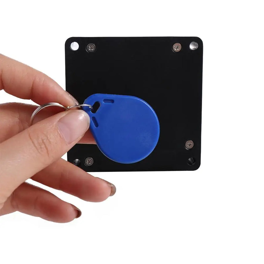 Hand holding blue RFID tag key fob in front of black hidden electronic drawer lock reader plate