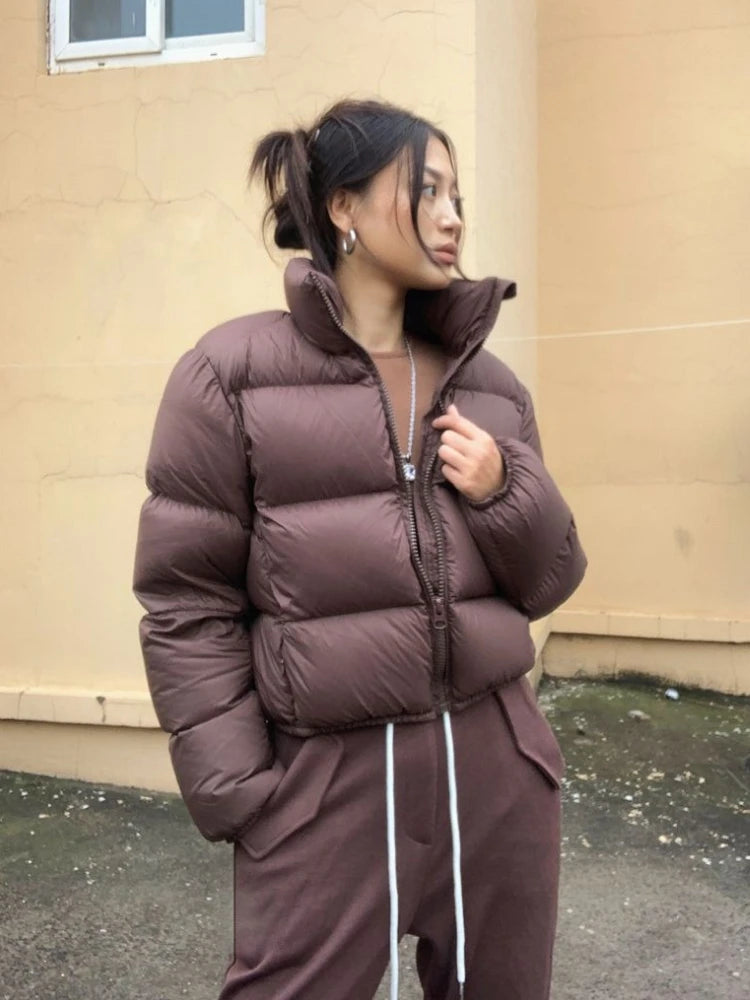 Person wearing a brown cropped puffer jacket and pants standing against a beige wall