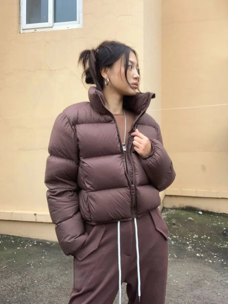 Person wearing a brown cropped puffer jacket and pants standing against a beige wall