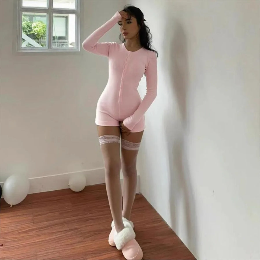 Full-body view of model wearing pink long sleeve button-front romper, standing in a room with balloons