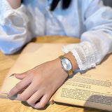 Hand wearing a gold watch on an open book with a light blue shirt
