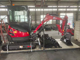 A red and black compact crawler excavator with a bucket attachment, photographed inside a large industrial warehouse or factory setting.