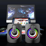 USB wired computer speakers with LED light displayed with a computer and smartphones in the background.