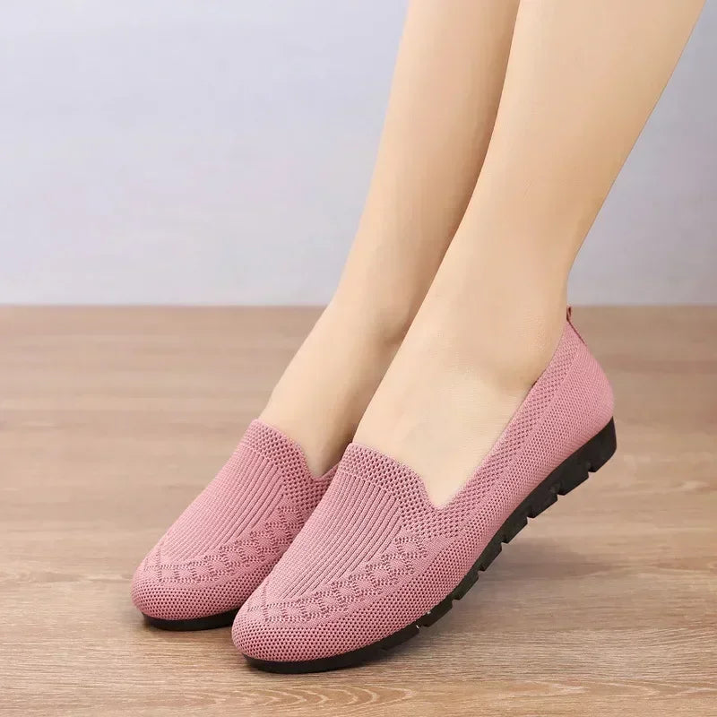 Pink slip-on shoes worn by a person on a wooden floor.