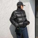Person wearing a black cropped puffer jacket and cap against a light-colored wall