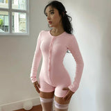 Model wearing pink long sleeve button-front romper with short legs and lace thigh-high stockings, standing near a window