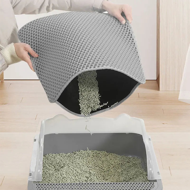 Person removing a gray double-layer cat litter trapping mat from a litter box on a wooden floor, easy-clean design