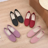 Set of four loafers in black, red, purple, and pink on a wooden floor.