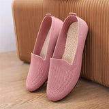 Pink loafers on a wooden floor with a brown suitcase in the background