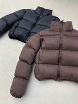 Two cropped puffer jackets, one black and one brown, on a light gray surface