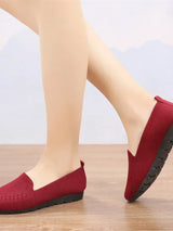 Red loafers worn with light-colored pants on a wooden floor.