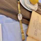 Gold watch on a textured surface with a book and lemon