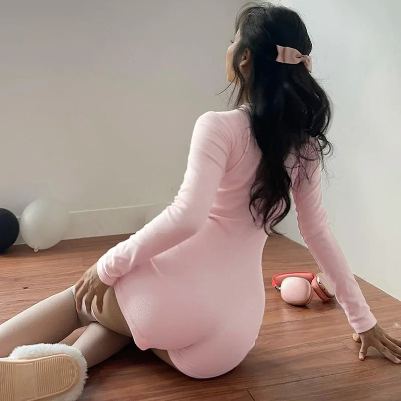 Model sitting on a wooden floor wearing pink long sleeve romper with short legs and pink bow in hair, headphones nearby