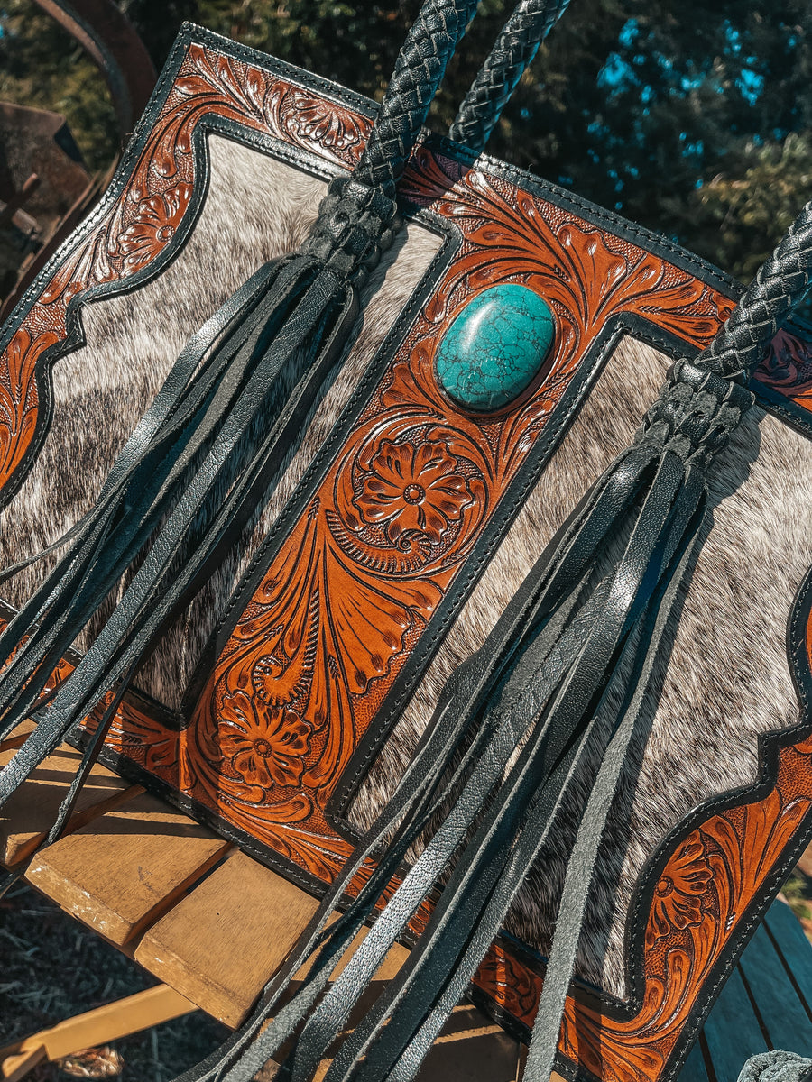 Close-up of tooled leather and cowhide western handbag with turquoise stone and black fringe tassels