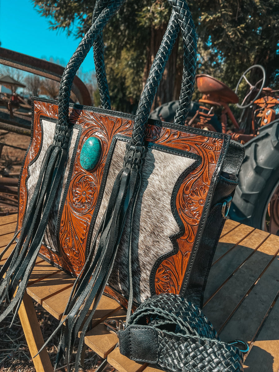 Handcrafted leather bag with turquoise stone and fringe details on a wooden surface.