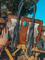 Handcrafted leather bag with braided handles and turquoise stone, outdoors.