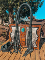 Handbag with braided handles and decorative leatherwork on a wooden surface with a rustic background.