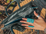 Hand with turquoise ring opening a black handbag on a wooden surface